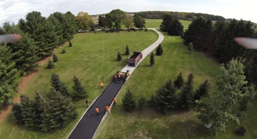 Paving a winding driveway in a green, rural setting; asphalt being laid by a crew with machinery.