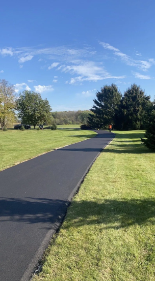 Black asphalt driveway through green grass under a blue sky.