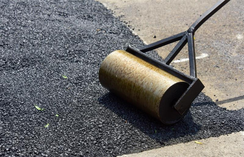 Asphalt being compacted with a hand roller on a paved surface.