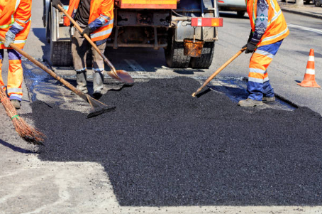 Road workers spreading asphalt on a street using rakes and brooms, next to a truck.