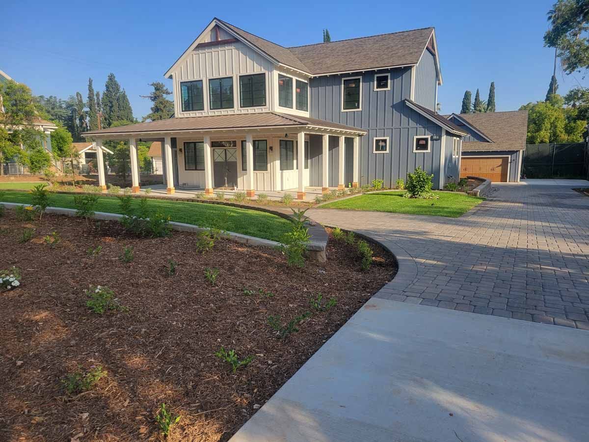 Blue farmhouse with a white porch, a driveway, and a landscaped yard.