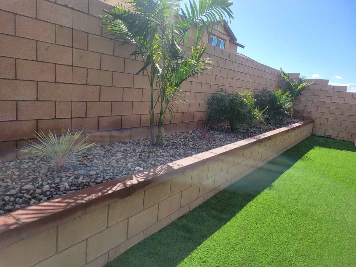 Brick wall with raised planter bed and palm trees, next to green turf lawn.
