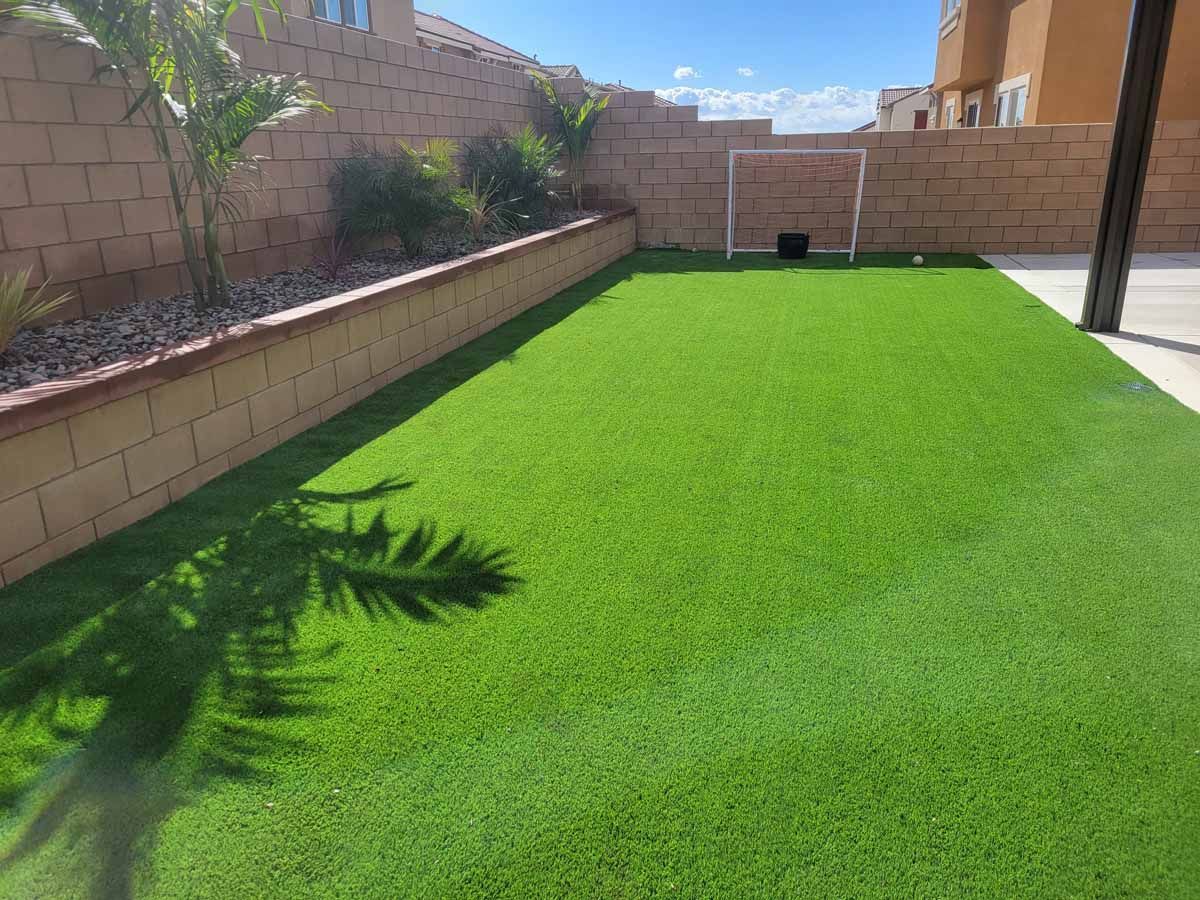 Bright green artificial turf backyard with a small soccer goal and brick walls.