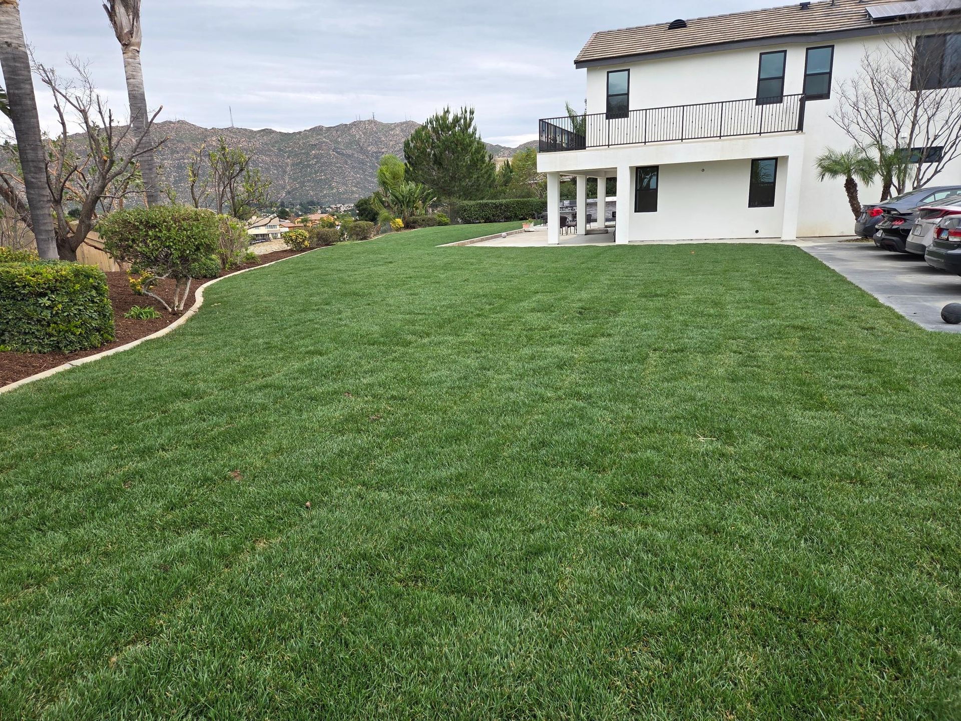 Green lawn in front of a white house with a mountain view.