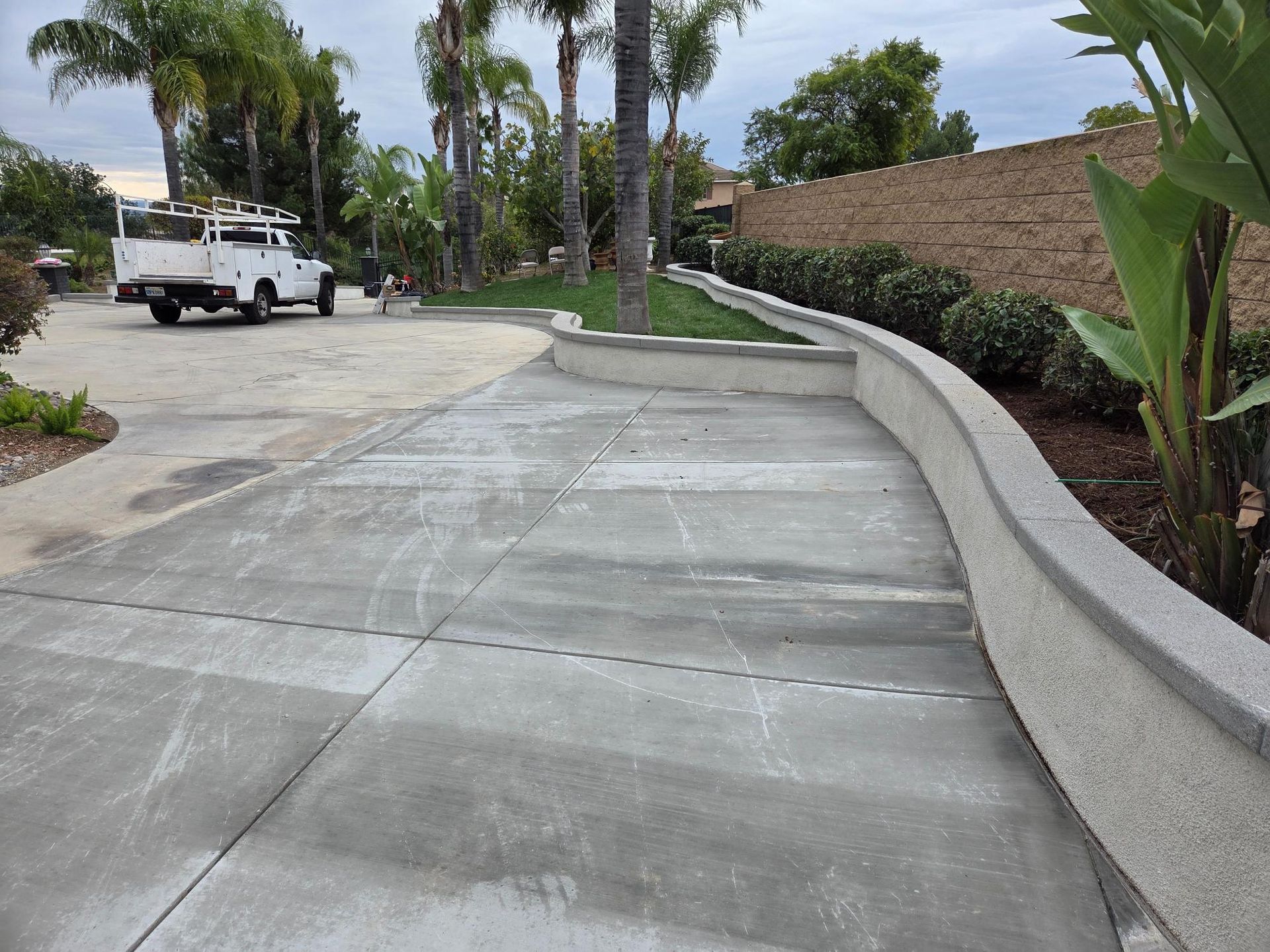 Concrete driveway with a stucco wall, truck parked in the distance, and green landscaping.