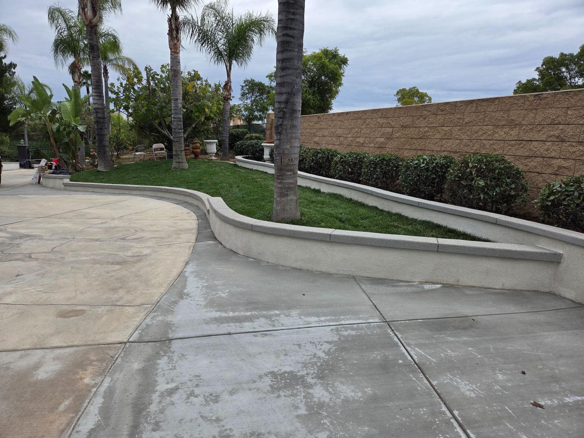 Concrete driveway curves around a raised planter with green grass and trees.
