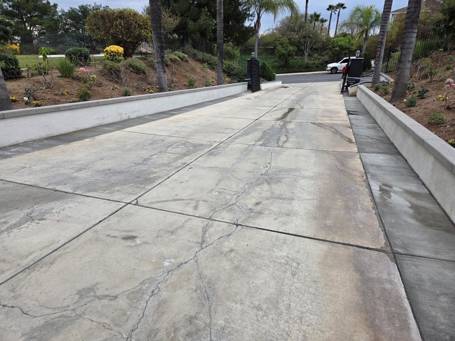 Concrete driveway with cracks, leading uphill. Palm trees and car in the background.