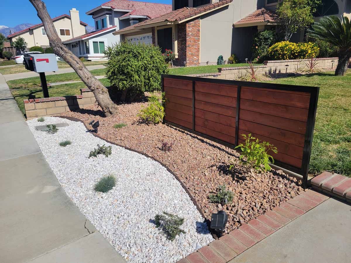 Front yard with a wooden privacy screen and a landscaped area with white rocks and small plants.