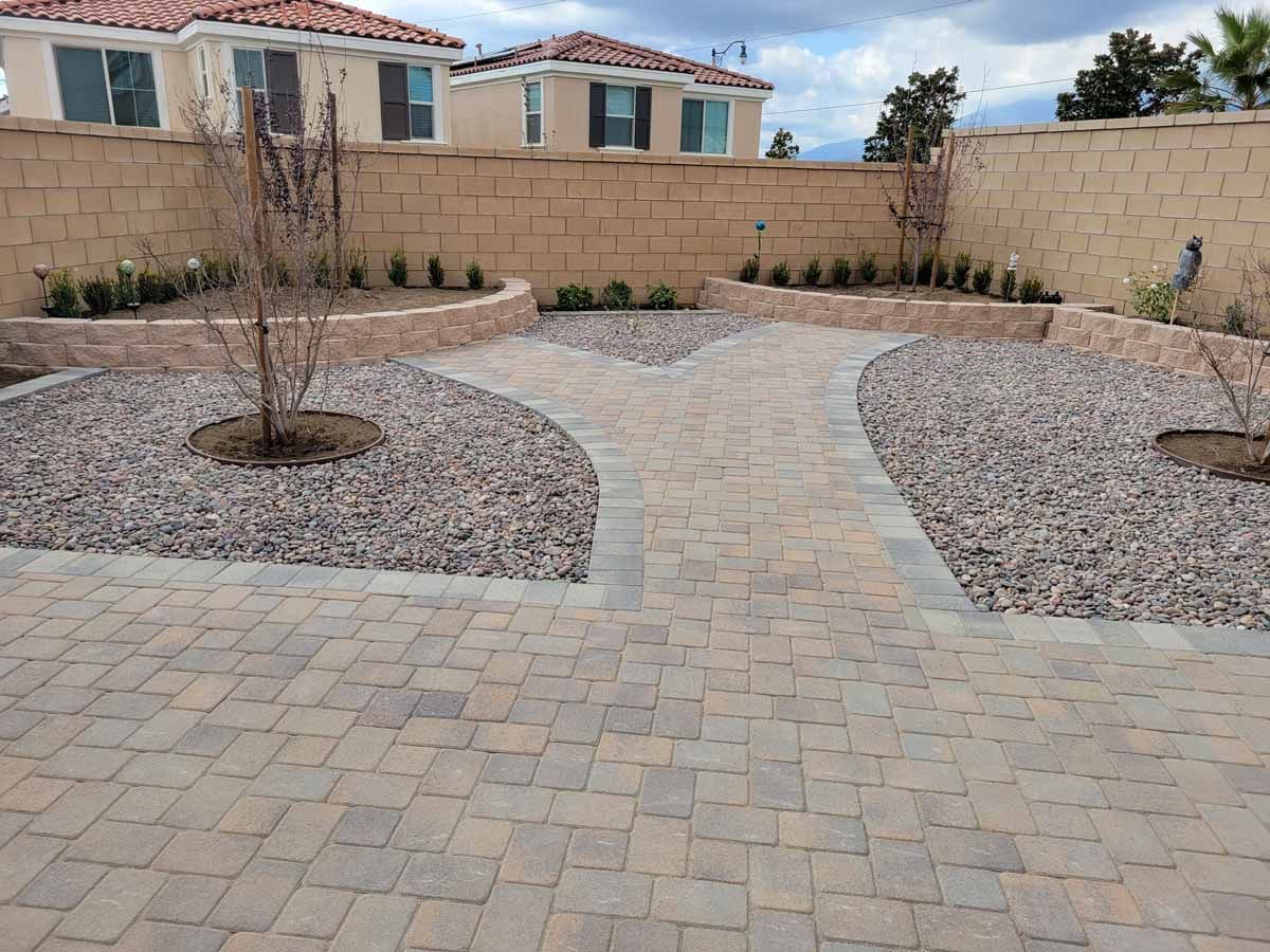 Brick patio with pathways leading through rock beds, with planting beds against a wall.