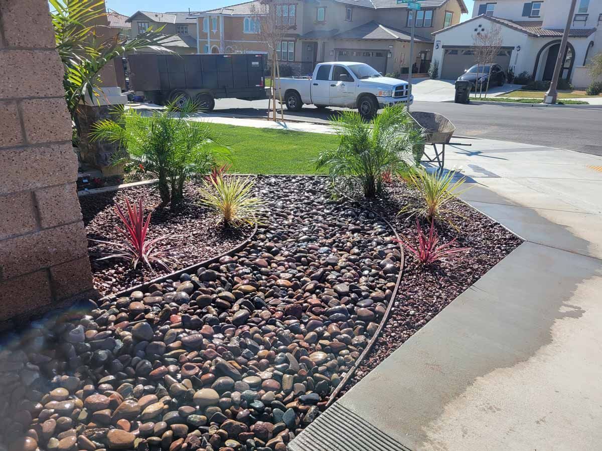 Landscaped front yard with dark rocks, plants, and a concrete walkway.
