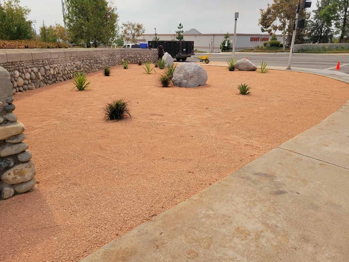 Landscaped area with reddish-brown mulch, large rocks, small plants, and a stone wall.