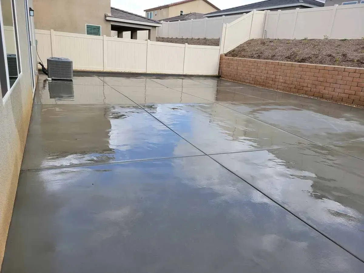 Wet concrete patio reflecting the sky. Beige walls surround the space.