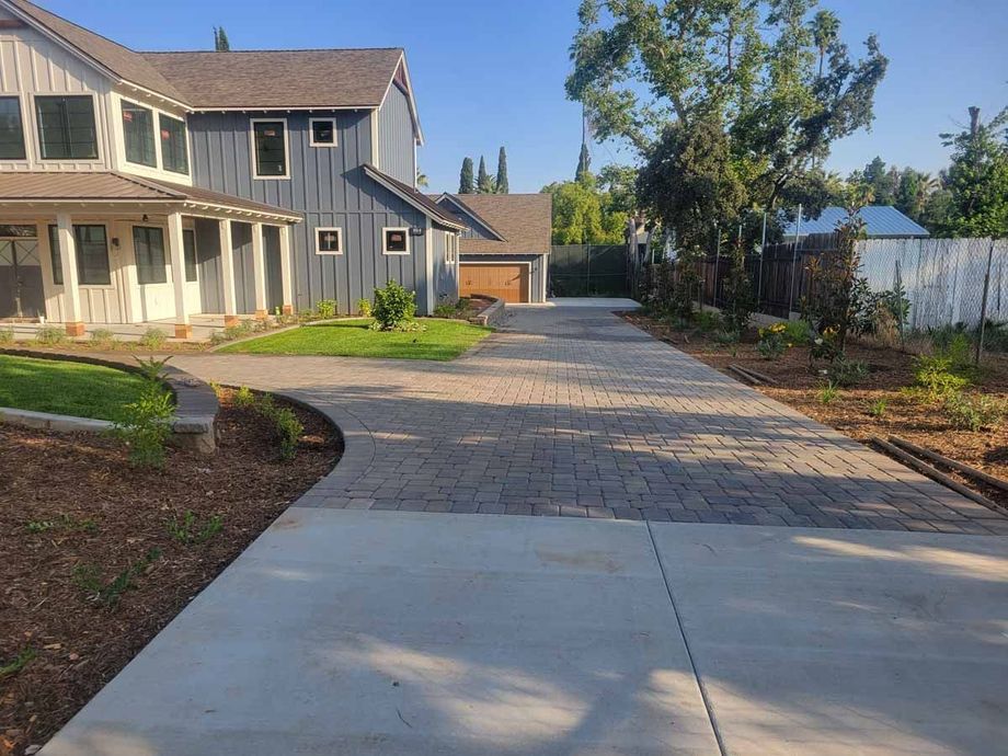 Driveway leading to a two-story blue house and a detached garage, under a bright sky.