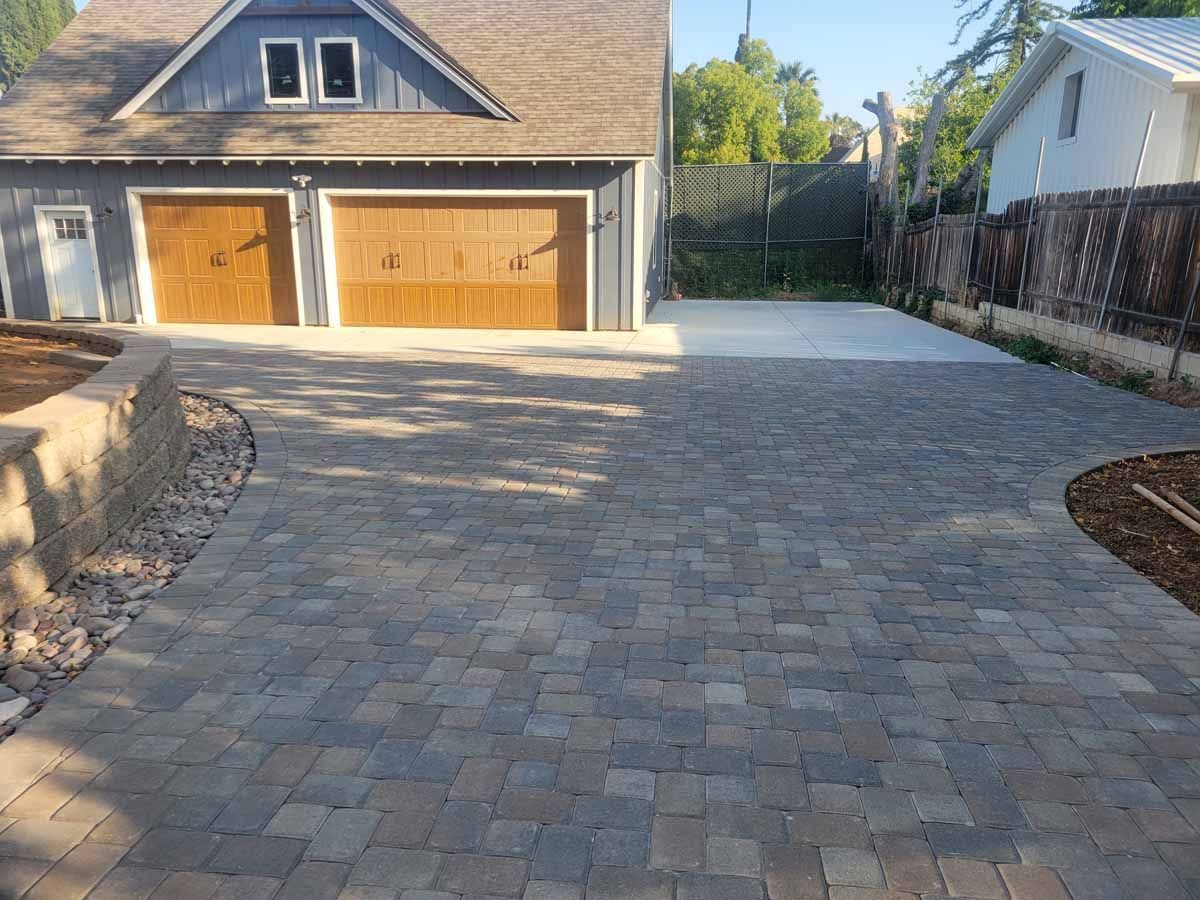 Brick paver driveway leading to a blue garage with brown doors, next to a white house.