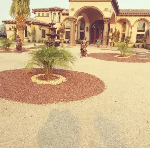 Elegant house with fountain and palm trees in gravel yard.