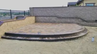 Stone patio with curved steps and retaining walls, surrounded by sand.