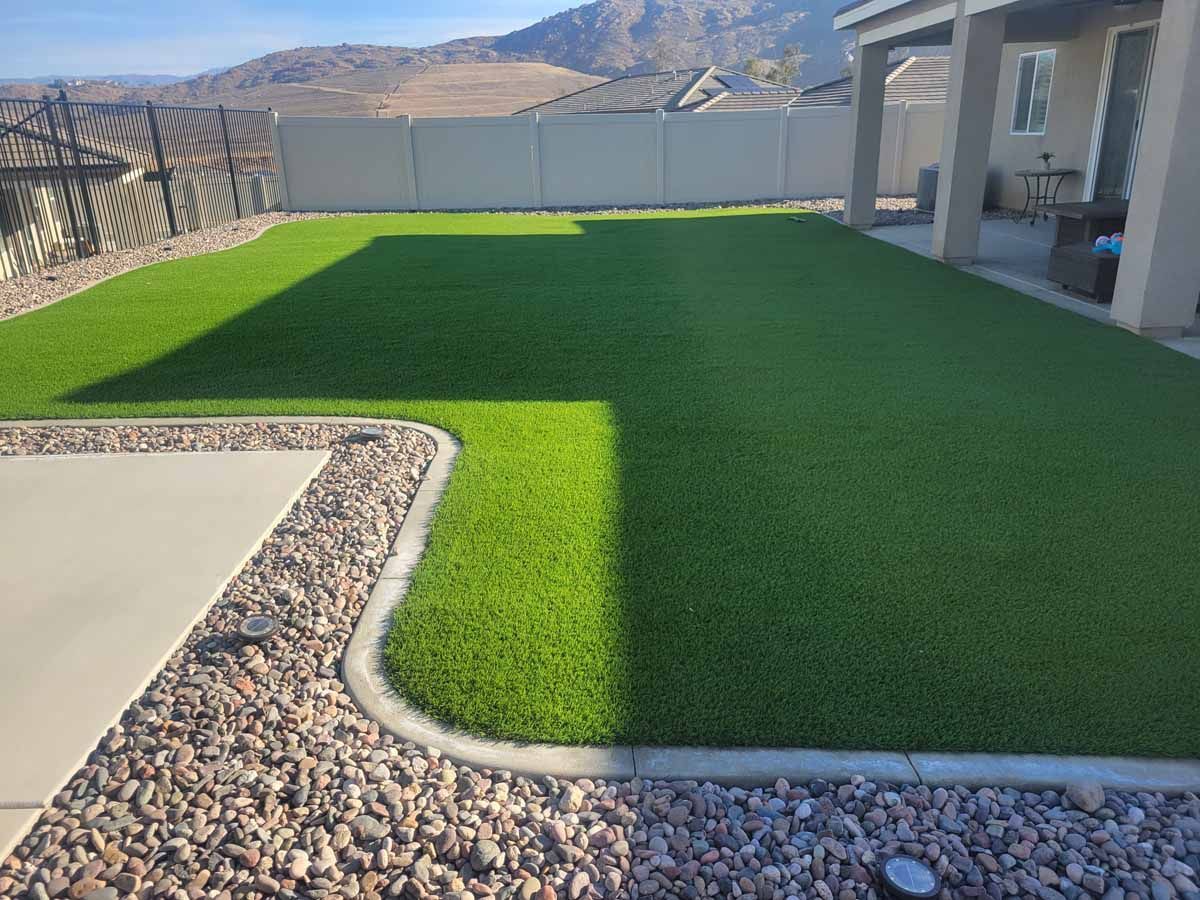 Backyard with green turf, concrete patio, gravel border, and mountains in the background.