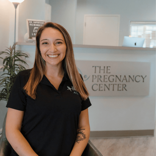 A woman is standing in front of a sign that says the pregnancy center