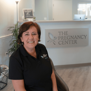 A woman is sitting in front of a sign that says the pregnancy center