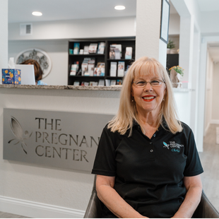 A woman is sitting in front of a sign that says the pregnant center