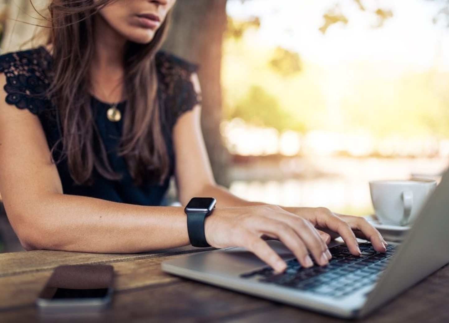 A woman is sitting at a table typing on a laptop computer.