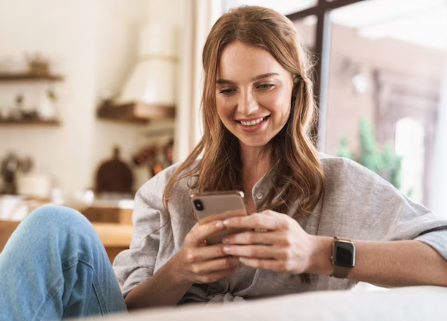 A woman is sitting on a couch looking at her cell phone.