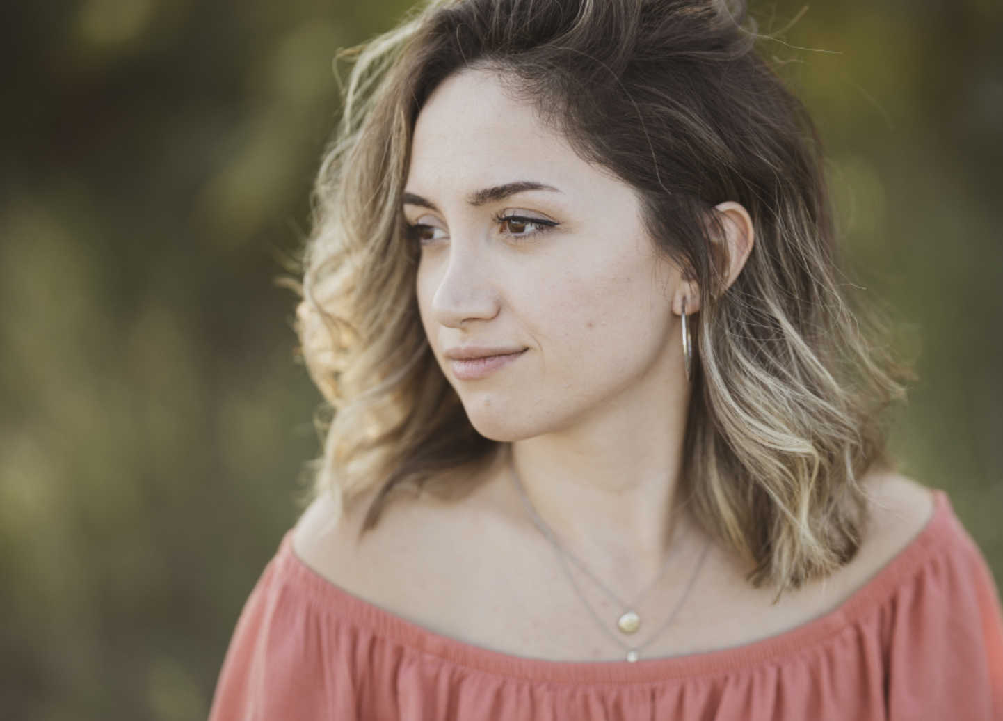 The woman is wearing a red off the shoulder top and a necklace.