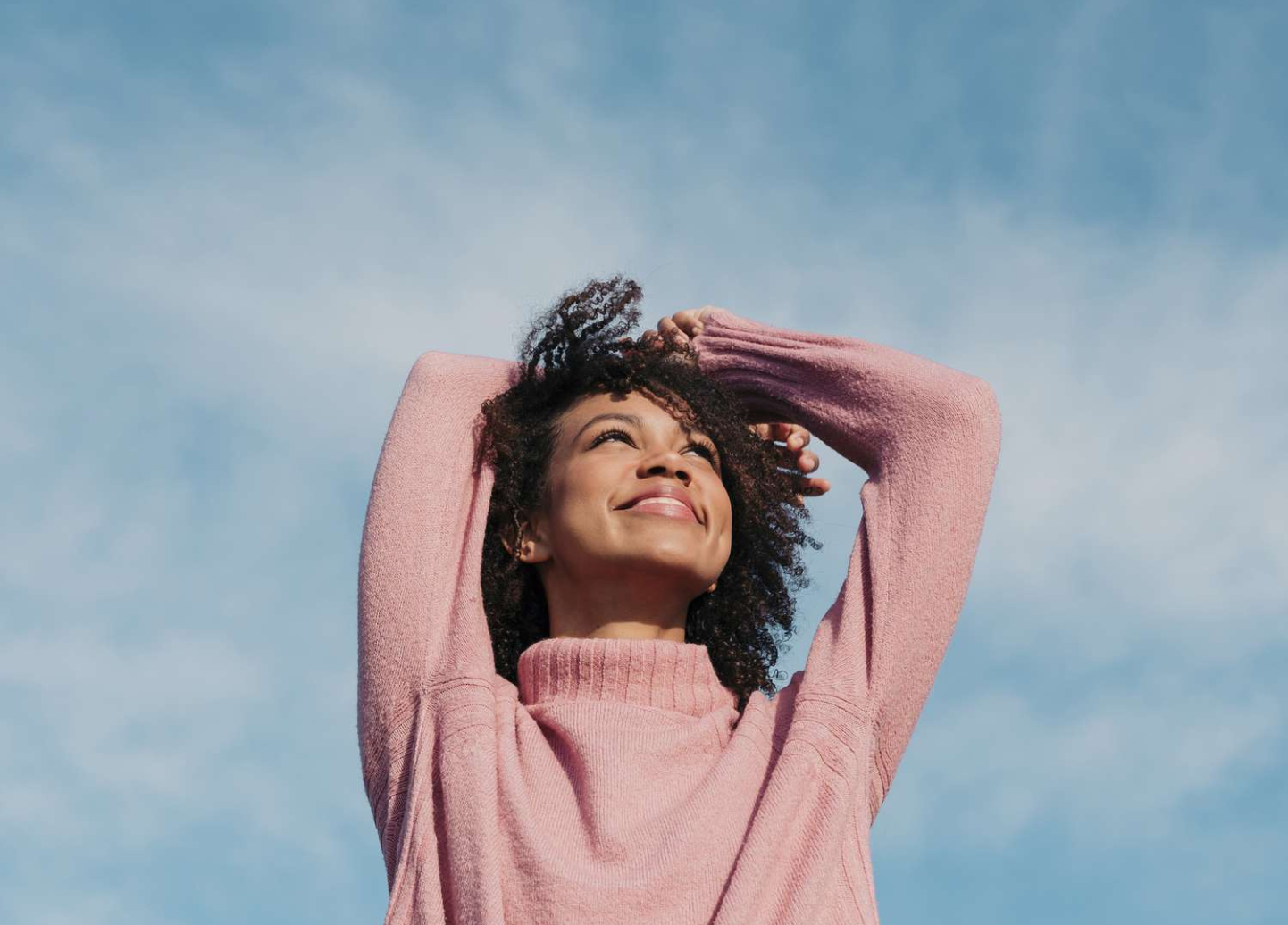 A woman in a pink sweater is looking up at the sky.