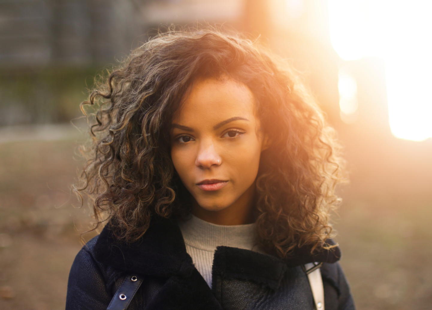 A woman with curly hair is wearing a black coat and looking at the camera.