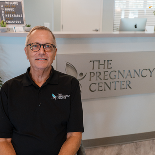 A man is sitting in front of a sign that says the pregnancy center