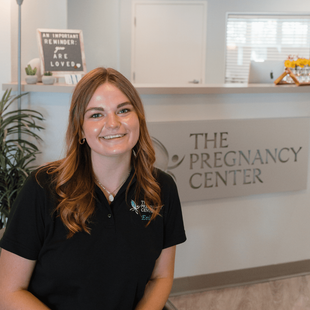 A woman is sitting in front of a sign that says the pregnancy center