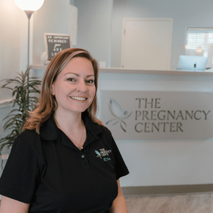 A woman is smiling in front of a sign that says the pregnancy center