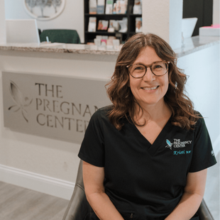 A woman is sitting in front of a sign that says the pregnancy center