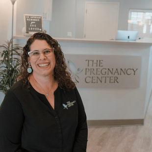 A woman is smiling in front of a sign that says the pregnancy center