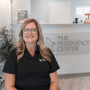 A woman is sitting in front of a sign that says the pregnancy center