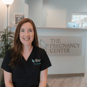 A woman is sitting in front of a sign that says the pregnancy center