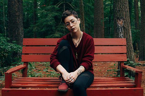 A woman is sitting on a red bench in the woods.