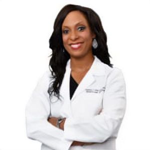 A woman in a white lab coat with her arms crossed is smiling.