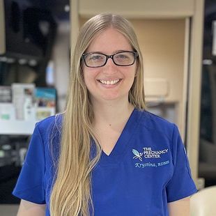 A woman wearing glasses and a blue scrub top is smiling for the camera.