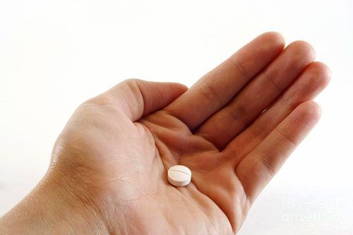 A person is holding a small white pill in their hand.