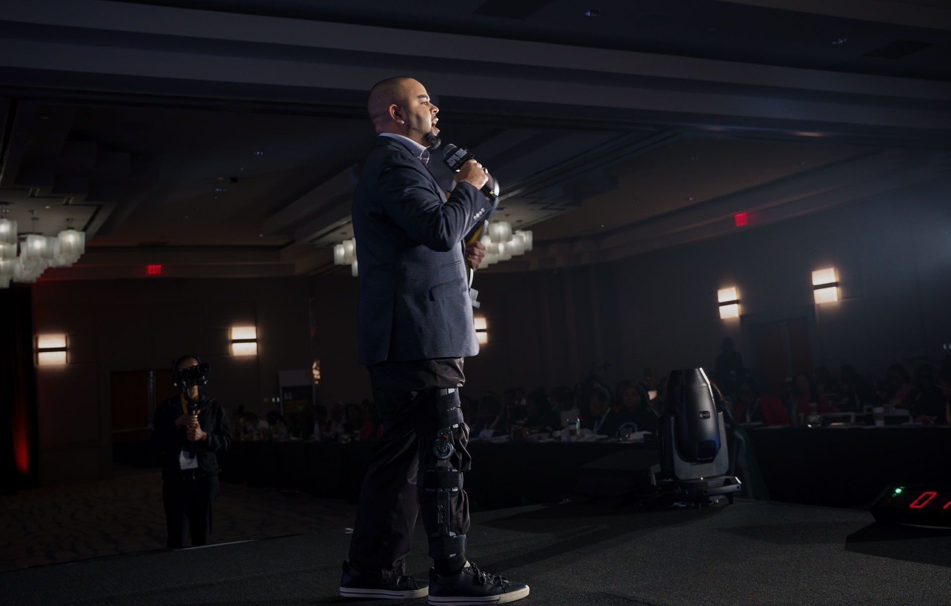 A man is standing in front of a microphone in a dark room.