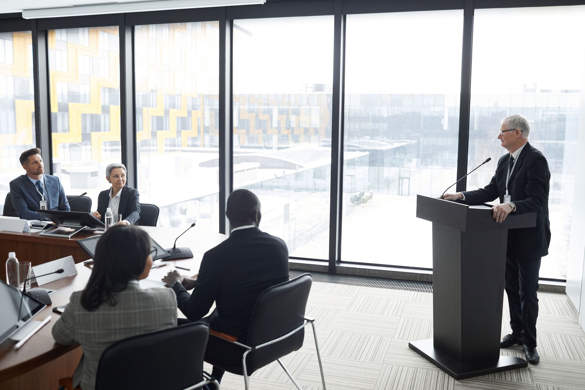 Business presentation in a conference room, with a speaker at a podium addressing seated attendees.
