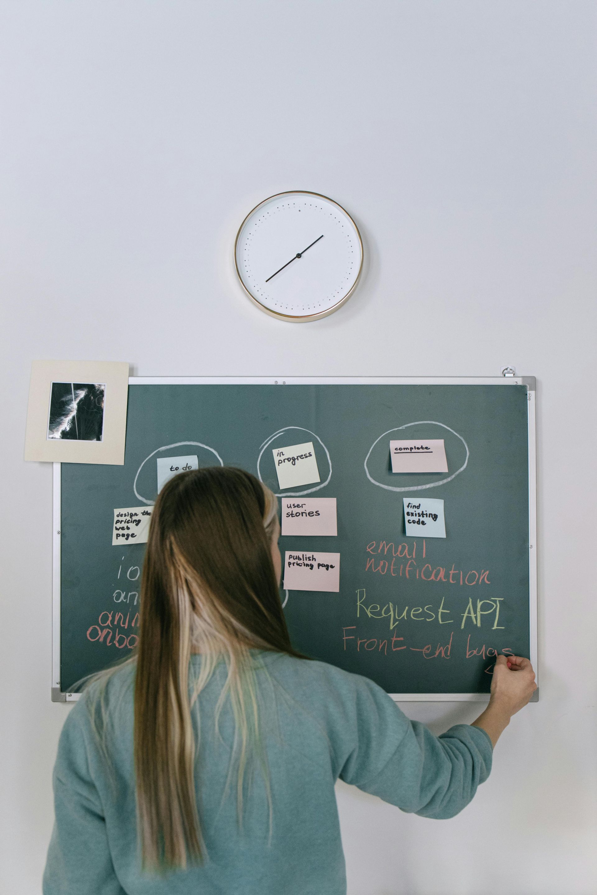 A woman is writing on a blackboard in front of a clock.