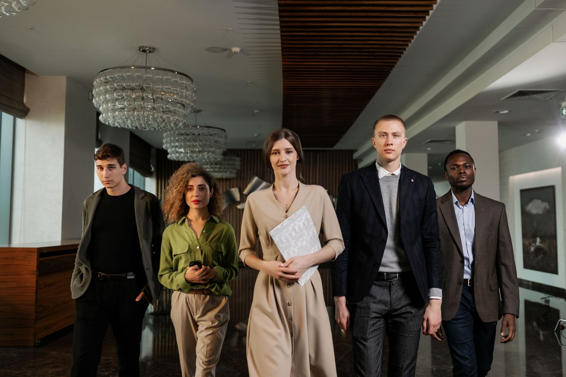 Five professionals walking through a modern office lobby, led by a woman in white.