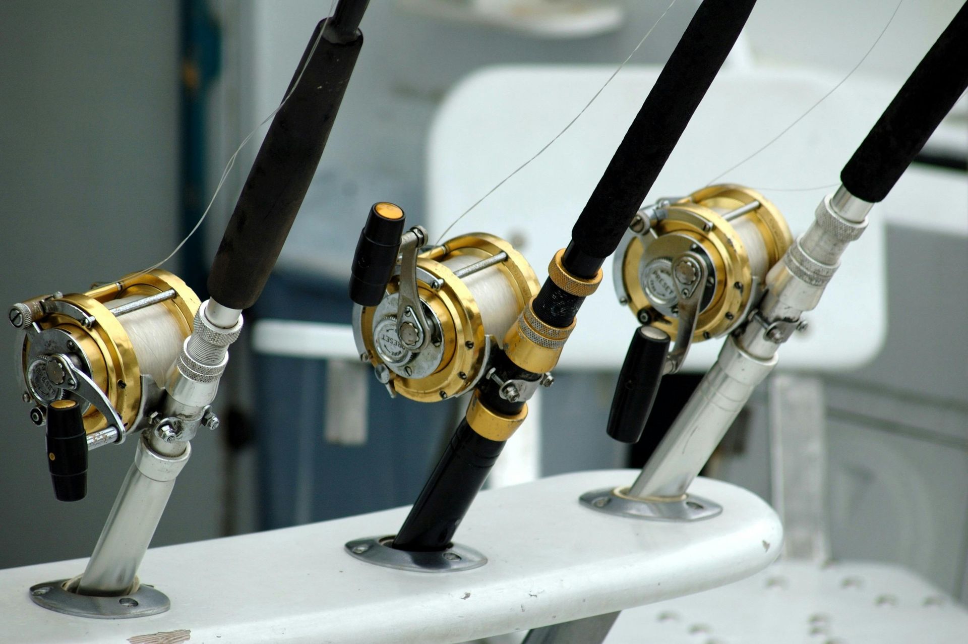 Three gold and silver fishing reels mounted on a white boat surface.