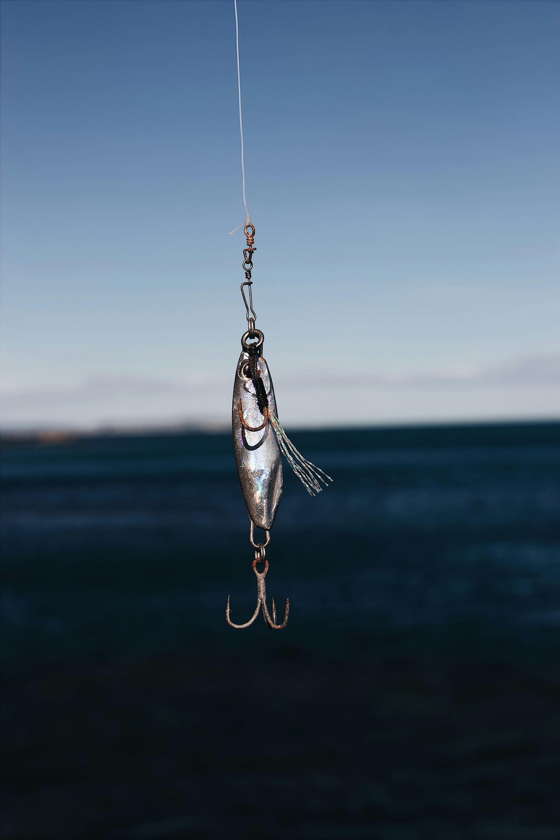 Fishing lure hanging against a blue sky and ocean background.