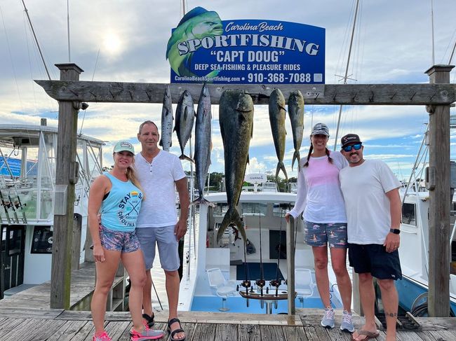 Four people posing with caught fish on a dock under a sign for 