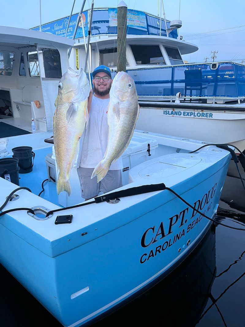 Man holding two large fish on a blue fishing boat; 