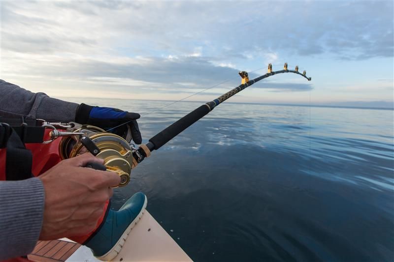 Angler holding a bent fishing rod on a boat, battling a fish in the ocean.