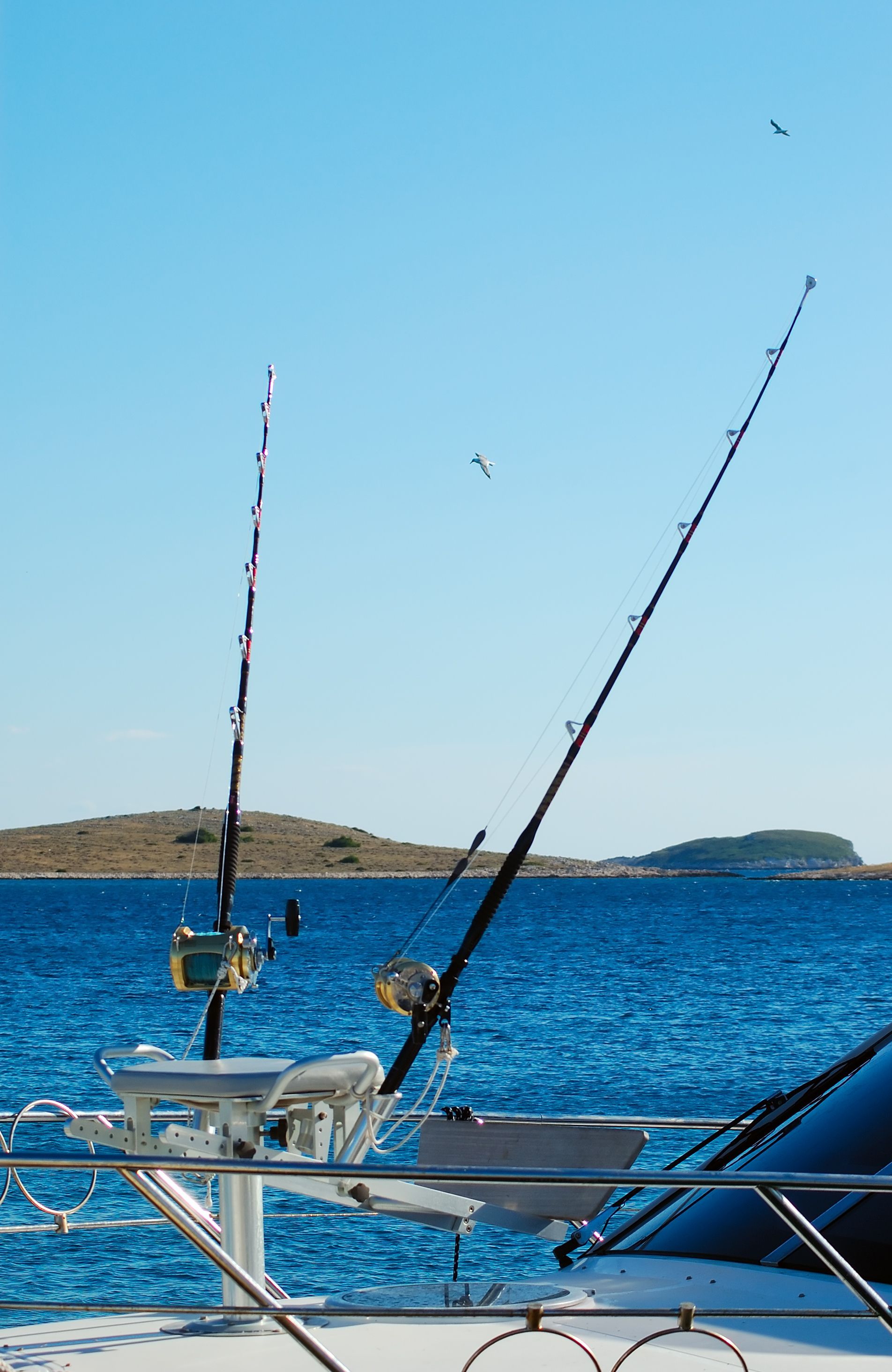 Fishing rods on a boat overlooking the ocean, blue sky, and islands.